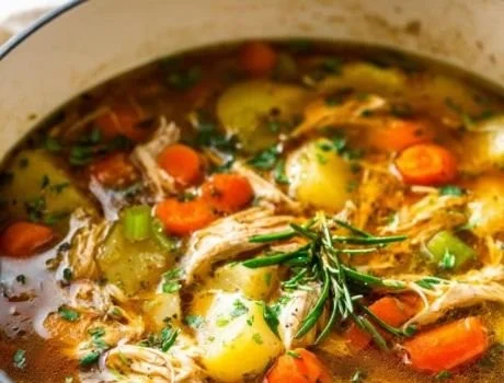 Bowl of hearty chicken veggie soup with fresh vegetables in a cozy kitchen setting.