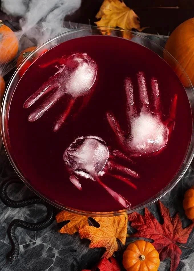 A glass of spooky Halloween party punch with eerie decorations.